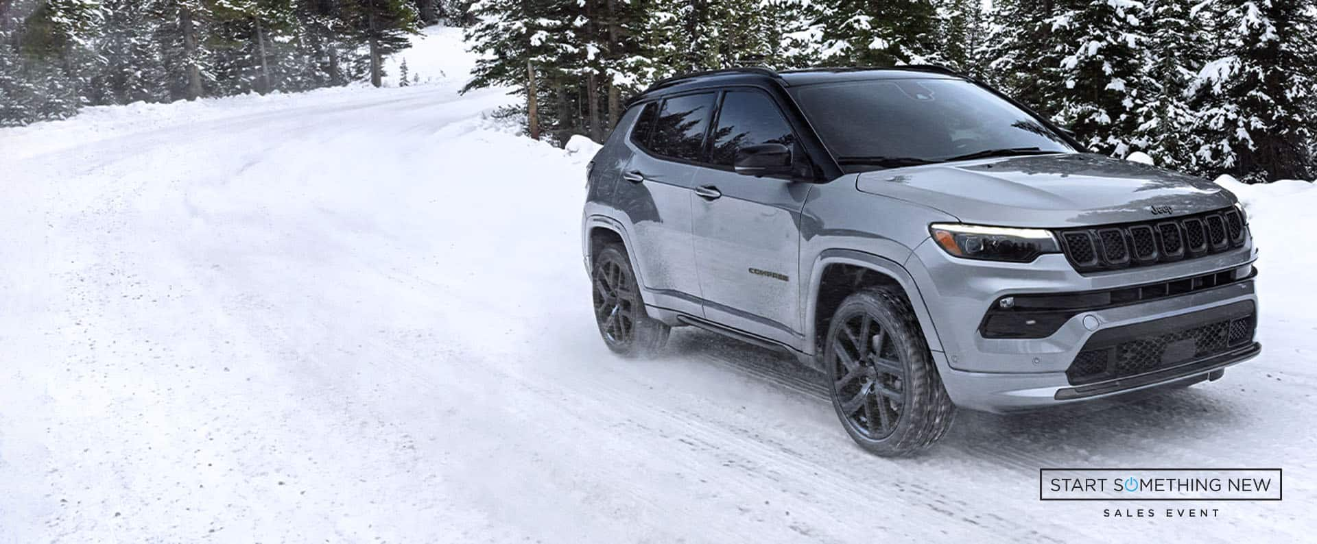 A silver 2025 Jeep Compass High Altitude, traveling on a snow-covered trail off-road in a forest. Start Something New Sales Event logo