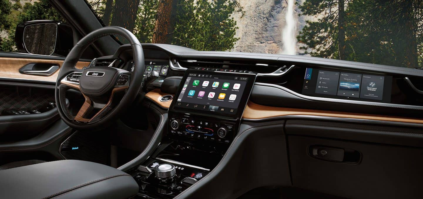 Display The interior of a 2025 Jeep Grand Cherokee Summit Reserve focusing on the steering wheel, Uconnect touchscreen, center stack and front passenger touchscreen.