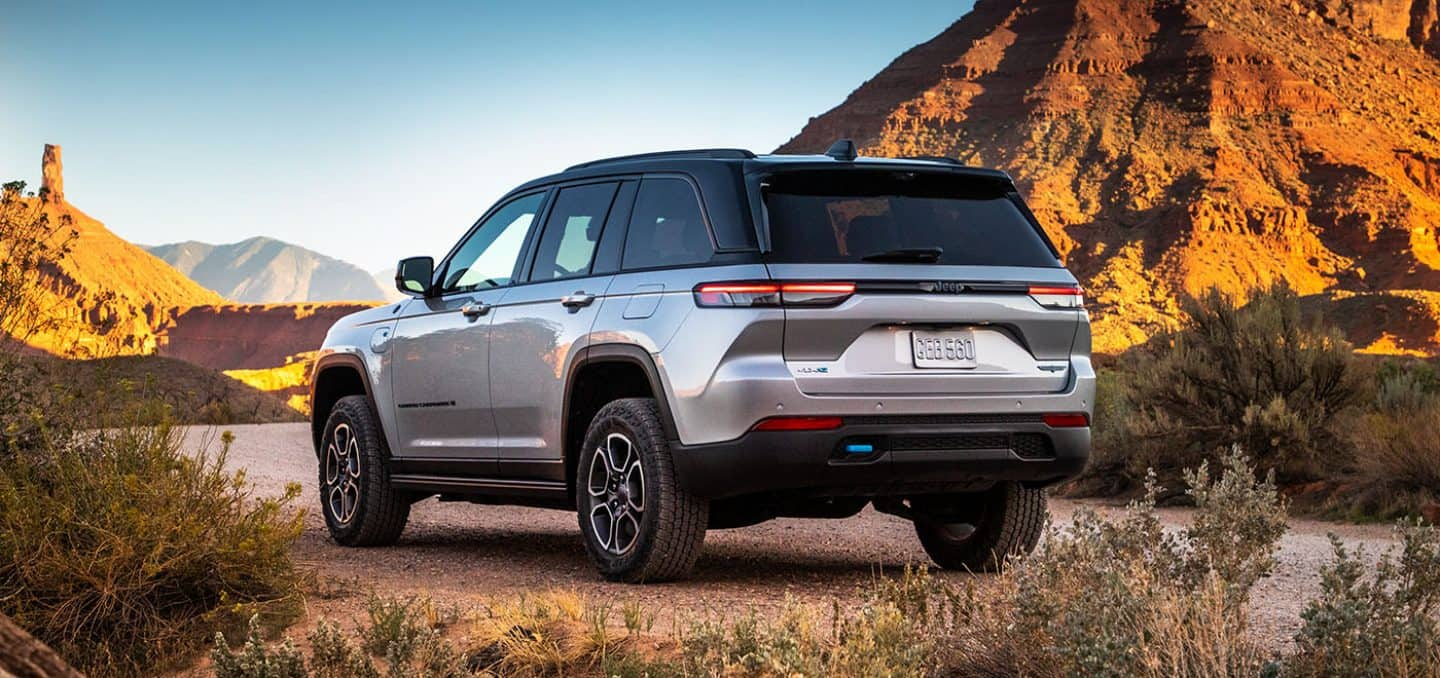 Display A silver 2025 Jeep Grand Cherokee Trailhawk 4xe parked on a clearing off-road, surrounded by hills of stone.