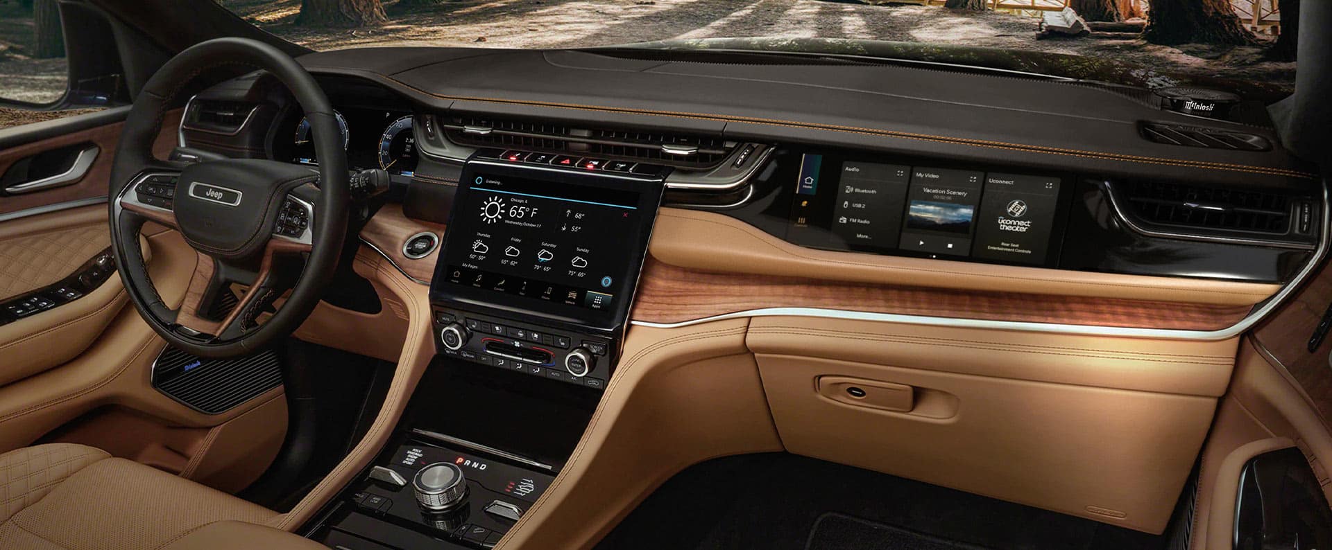 El volante, la pantalla táctil de Uconnect, la pantalla táctil interactiva del pasajero delantero, los controles de la consola central y la consola central en el Jeep Grand Cherokee Summit Reserve 2025.