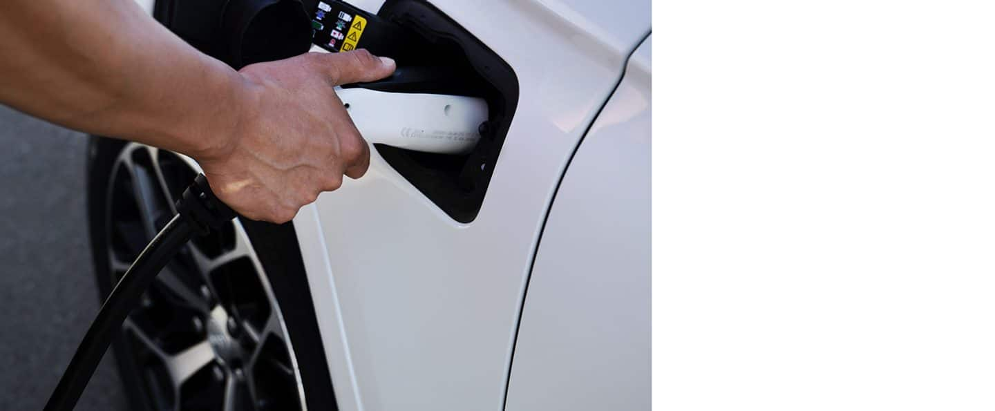 A man plugging a charging cord into the charging port on a white 2025 Jeep Grand Cherokee.