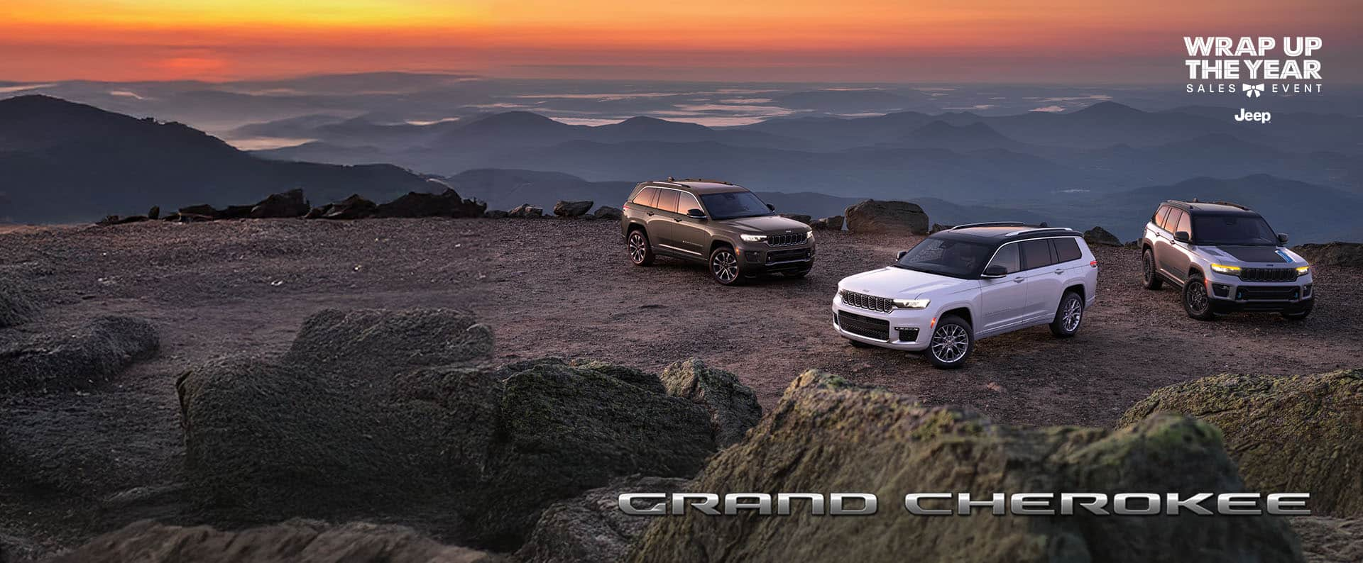 Three 2025 Jeep Grand Cherokee models parked on a rocky clearing at dusk, with mountains in the background; from left to right: a gray Grand Cherokee Overland, white Grand Cherokee Summit and silver Grand Cherokee Trailhawk 4xe with black hood insert. Grand Cherokee. Wrap Up the Year Sales Event.