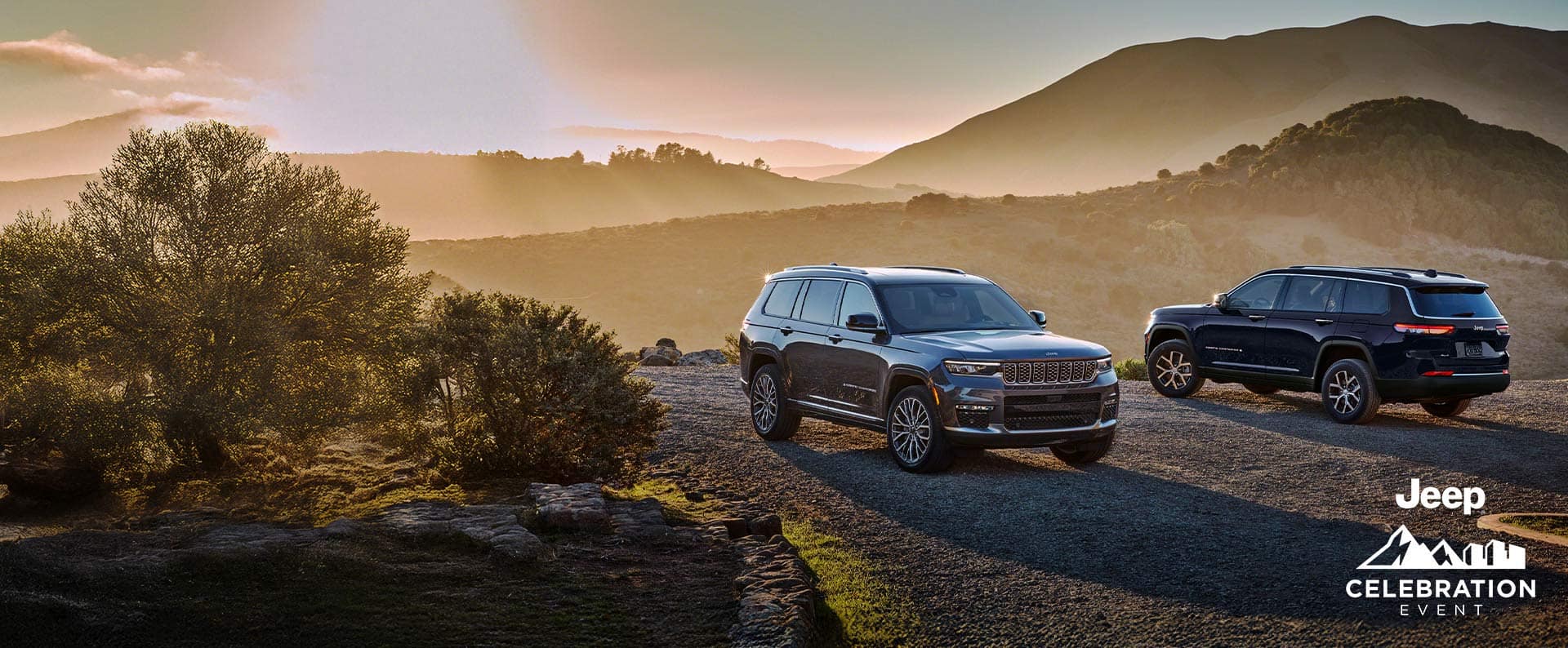 A gray 2025 Jeep Grand Cherokee Summit Reserve and a black 2025 Jeep Grand Cherokee Limited parked opposite of each other on a clearing in the mountains at sunset. The Jeep Celebration Event.