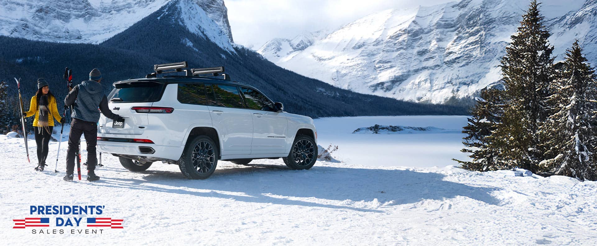 A white 2026 Jeep Grand Cherokee L High Altitude parked on a snow-covered clearing in the mountains. A couple nearby is carrying skiing equipment, and the man is about to open the liftgate. The Presidents' Day Sales Event.