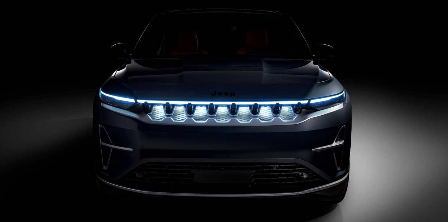 The front end of a black 2025 Jeep Wagoneer S Launch Edition with its headlamps on, parked in a darkened studio.