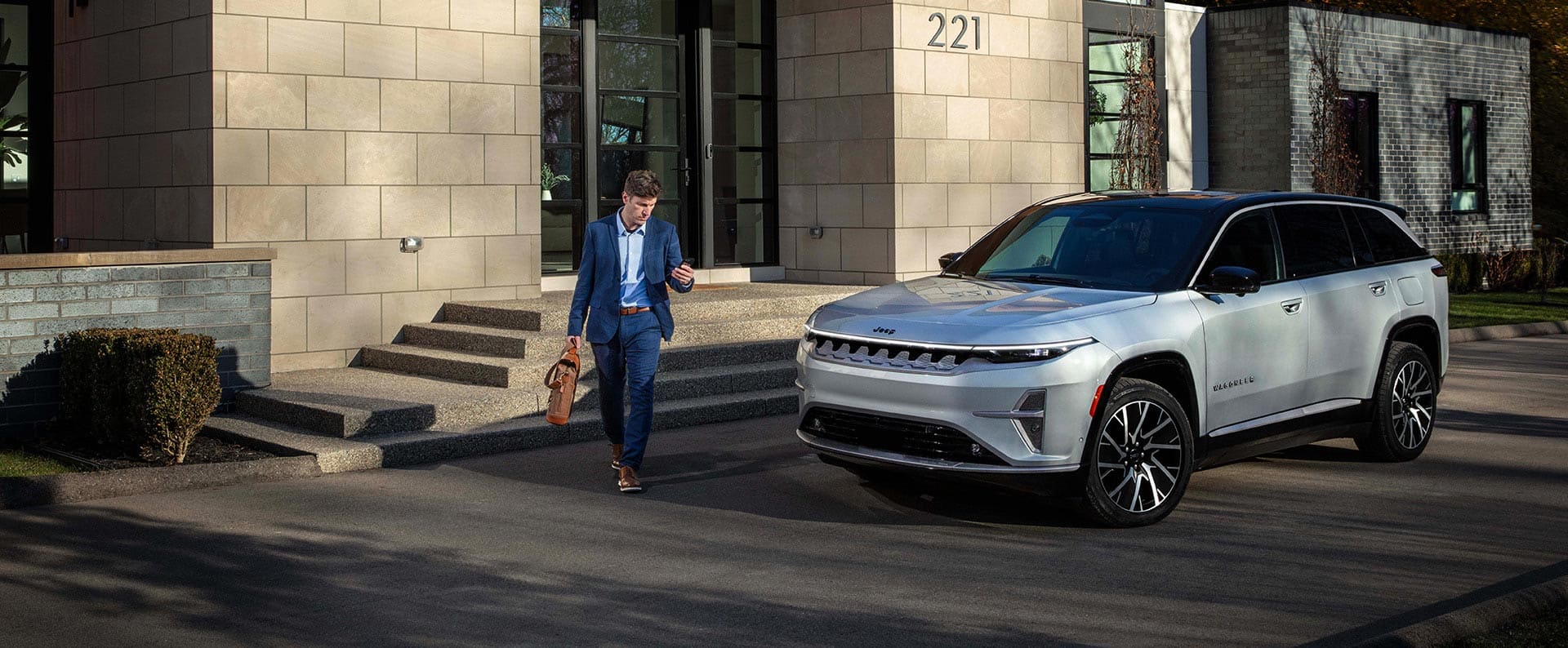 A silver 2025 Jeep Wagoneer S Limited parked in the driveway of a commercial building with a man walking nearby.