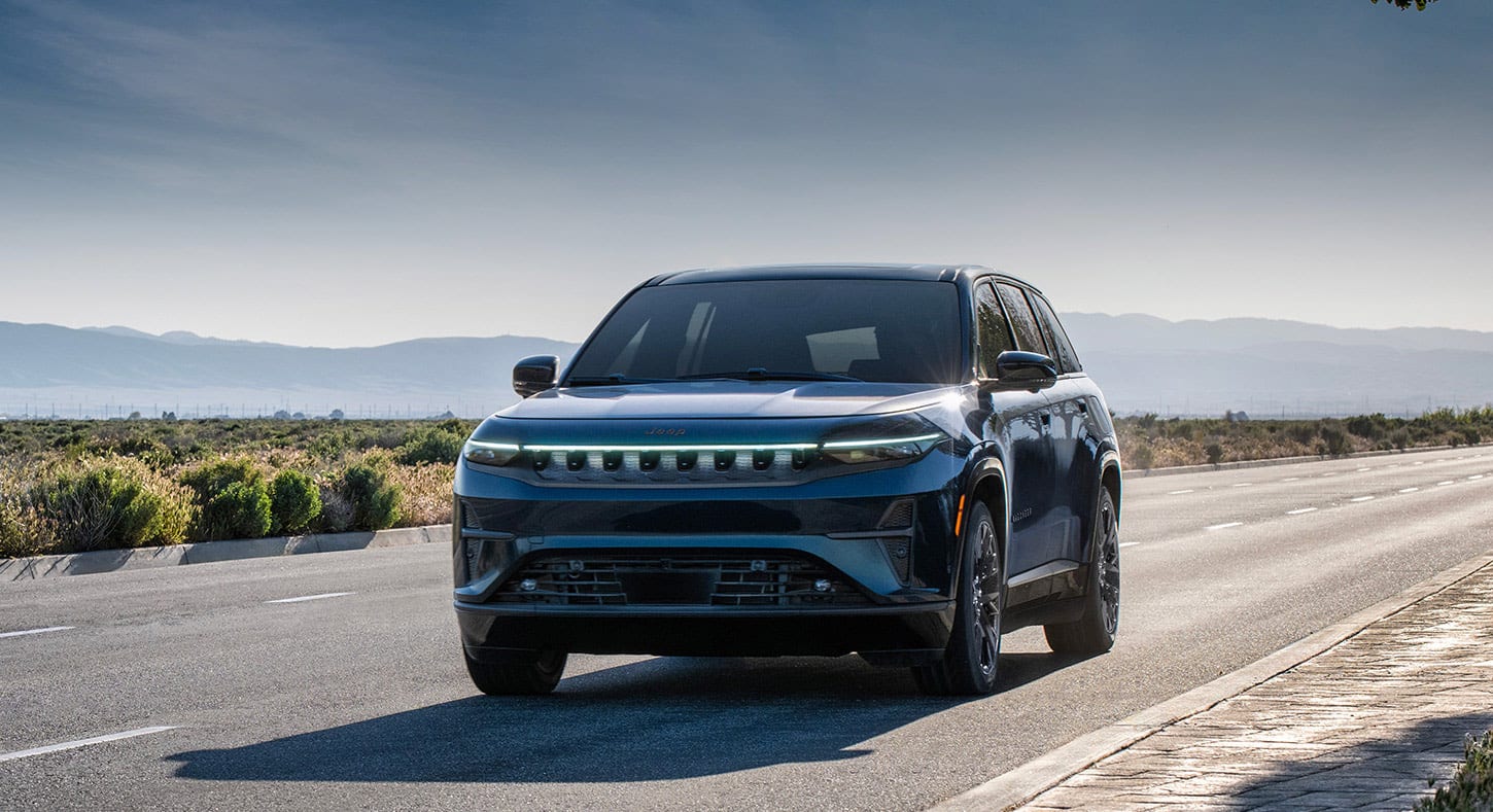 A blue 2025 Jeep Wagoneer S Launch Edition traveling on a desert highway with mountains in the background.