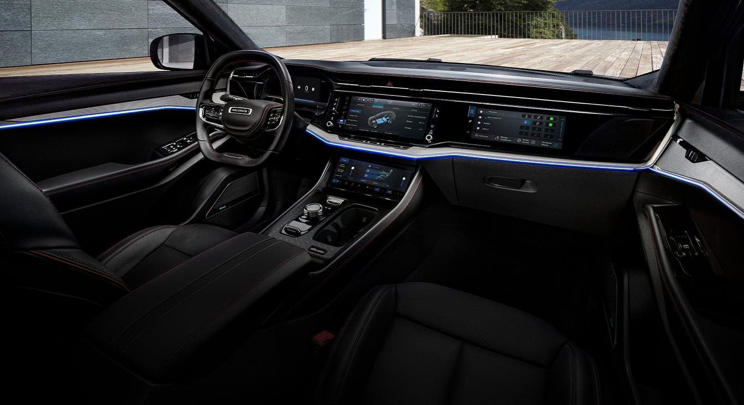 The front row in the 2025 Jeep Wagoneer S Launch Edition, focusing on the steering wheel, Digital Cluster Display, three touchscreens and ambient ribbon of blue light outlining the dash.