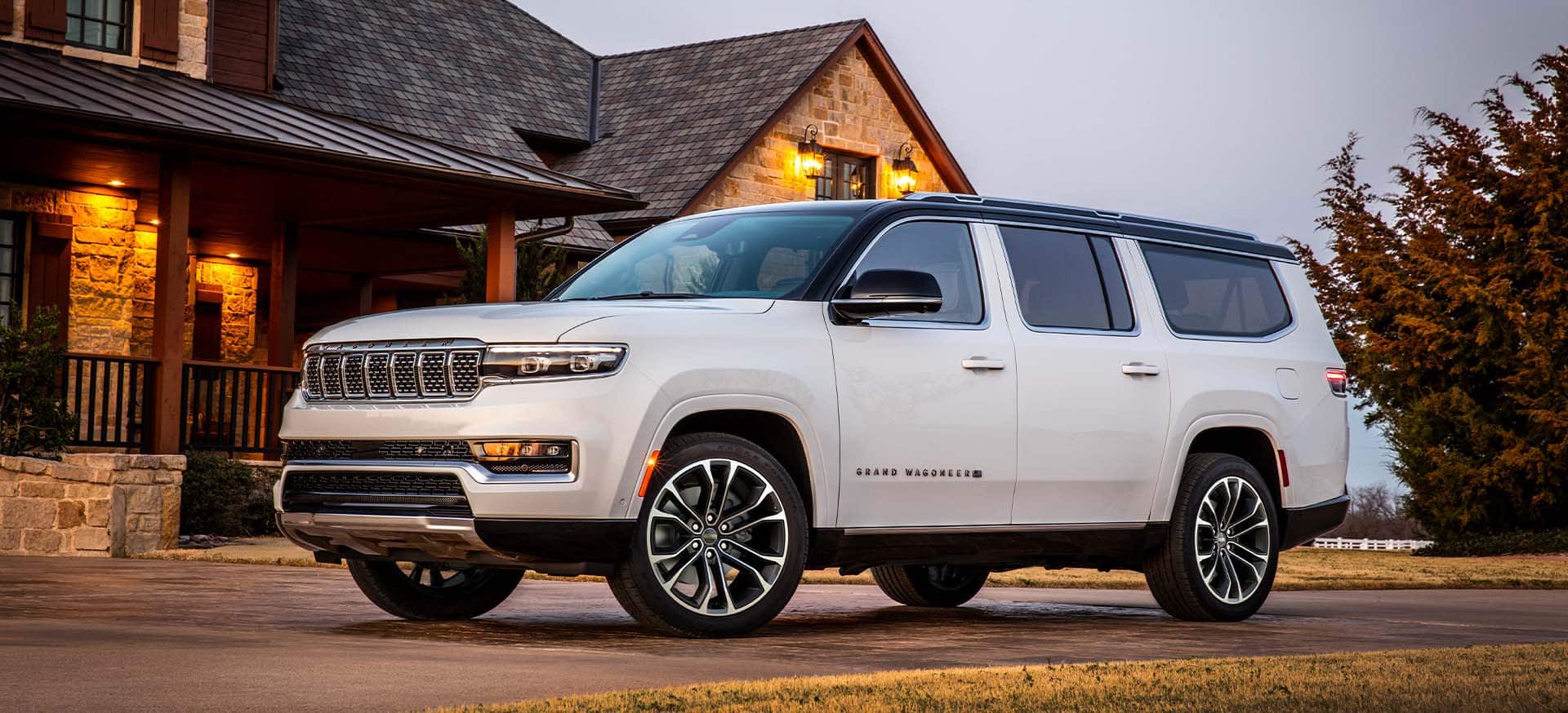 A driver-side front angle of a 2025 Jeep Grand Wagoneer Series 3 parked in the driveway of a large country home.