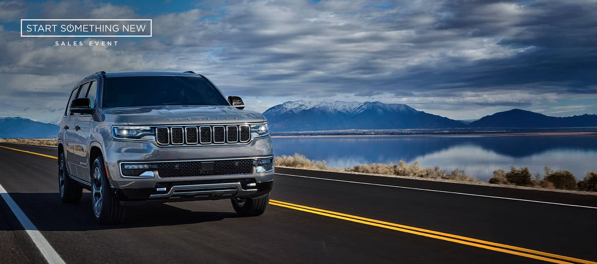 A silver 2025 Jeep Wagoneer Series III traveling on a highway beside a lake, with mountains in the background. Start Something New Sales Event logo.