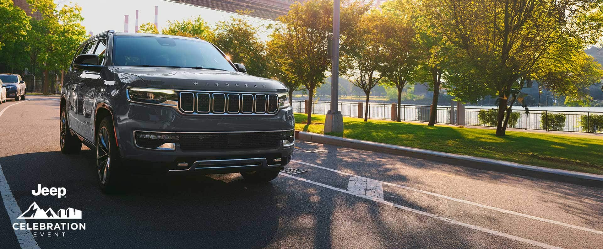 A gray 2025 Jeep Wagoneer Series 3 traveling on a city street along a riverfront. Jeep Celebration Event.