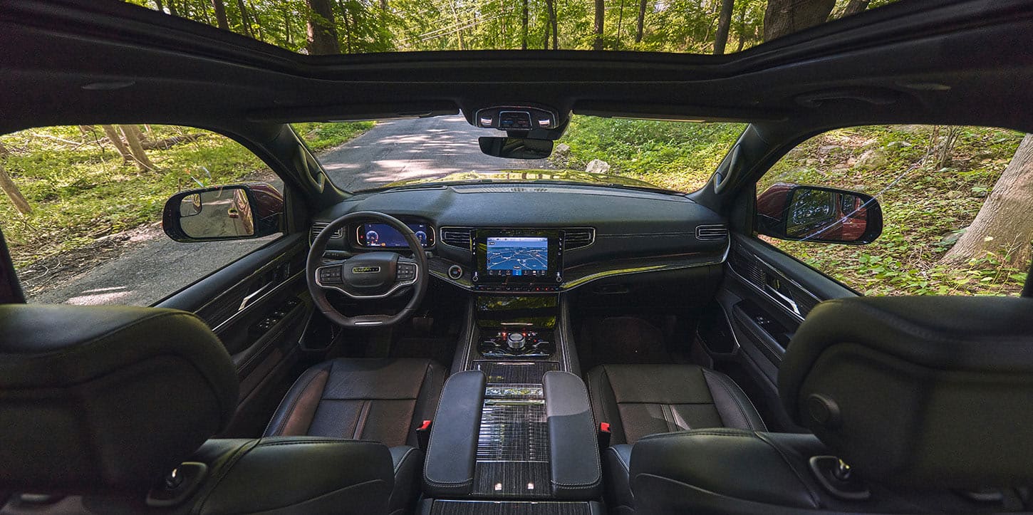 The front row of the 2025 Jeep Wagoneer Series III cabin, focusing on the seats, center console, steering wheel, Digital Cluster Display, Uconnect touchscreen center stack controls, dash and open sunroof.