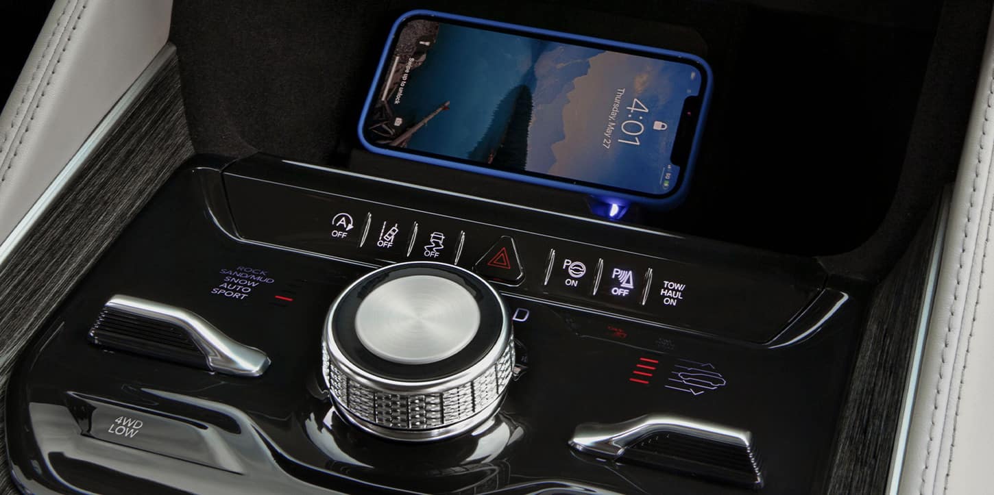 The center stack controls in the 2025 Jeep Wagoneer including the Selec-Terrain Traction Management System dial and the wireless charging pad with a smartphone on it.