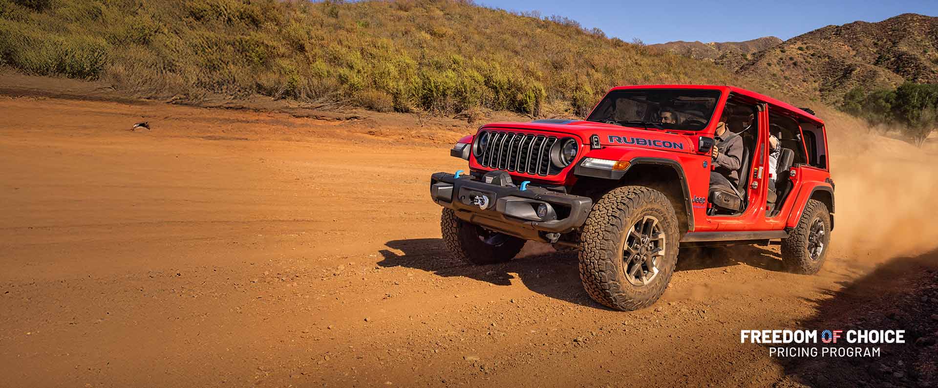A red 2025 Jeep Wrangler Rubicon X 4xe with its doors removed, climbing a sandy hill off-road. Freedom of Choice Pricing Program.