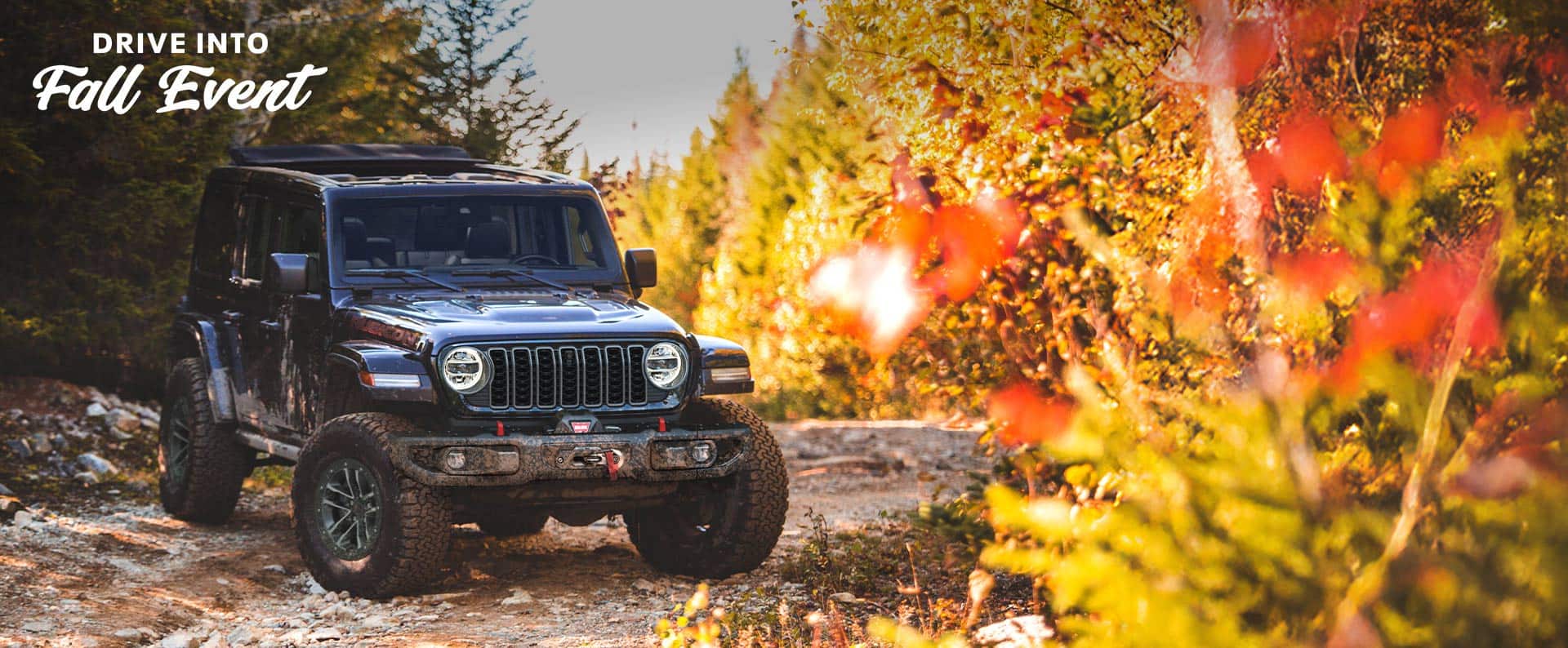 A black 2025 Jeep Wrangler Rubicon X parked on an off-road trail in the woods. The Drive Into Fall Event.