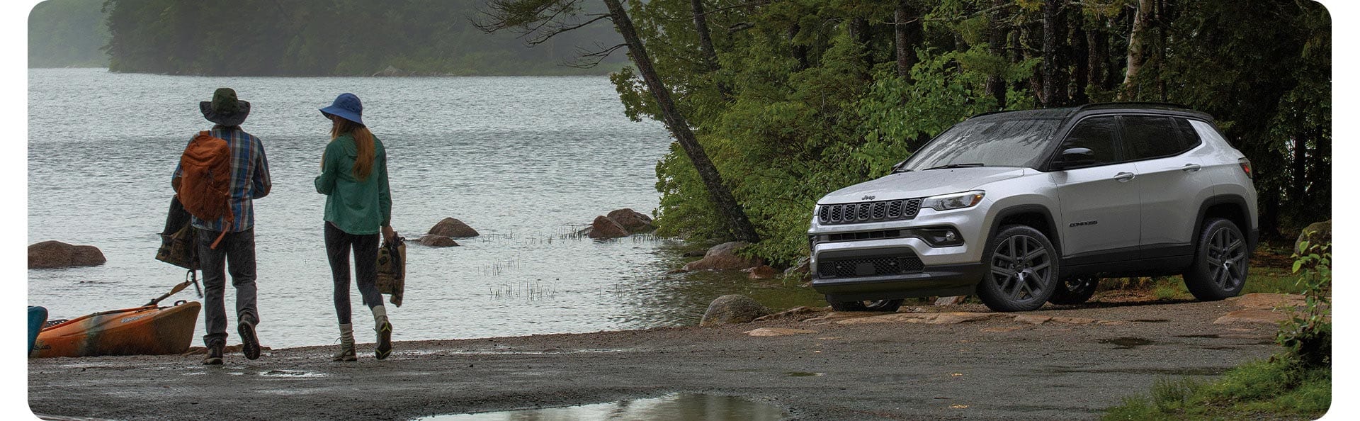 A silver 2026 Jeep Compass Limited Altitude, parked beside a lake, with a couple nearby.