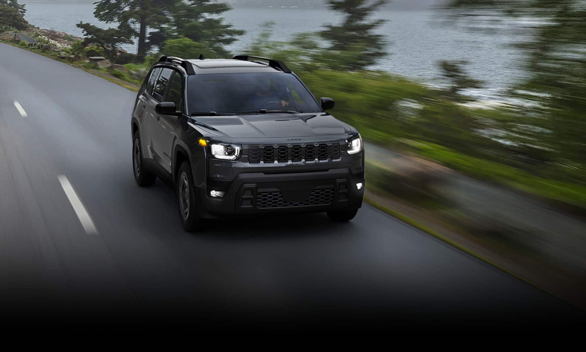 A black 2026 Jeep Cherokee Limited traveling down a highway beside a lake. The background is blurred to indicate the vehicle is in motion.