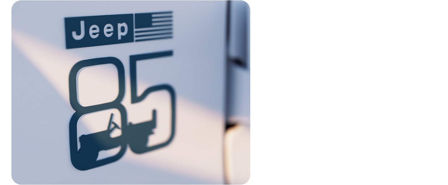 A close-up of the 85th Anniversary badge with the Jeep name and American flag on top and the number 85 below, with a silhouette profile of a Jeep Wrangler inside it.