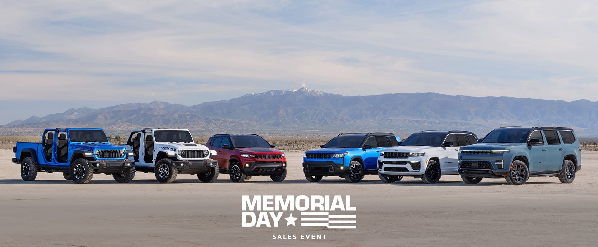 A lineup of six 2026 Jeep Brand vehicles parked in a semicircle. From left to right: a blue Gladiator Rubicon and white Wrangler Rubicon X—both with their doors and tops removed, a red Compass Trailhawk with black hood insert, a blue Cherokee Overland, a white Grand Cherokee Summit Obsidian, and a blue gray Grand Wagoneer Upland. Memorial Day Sales Event.
