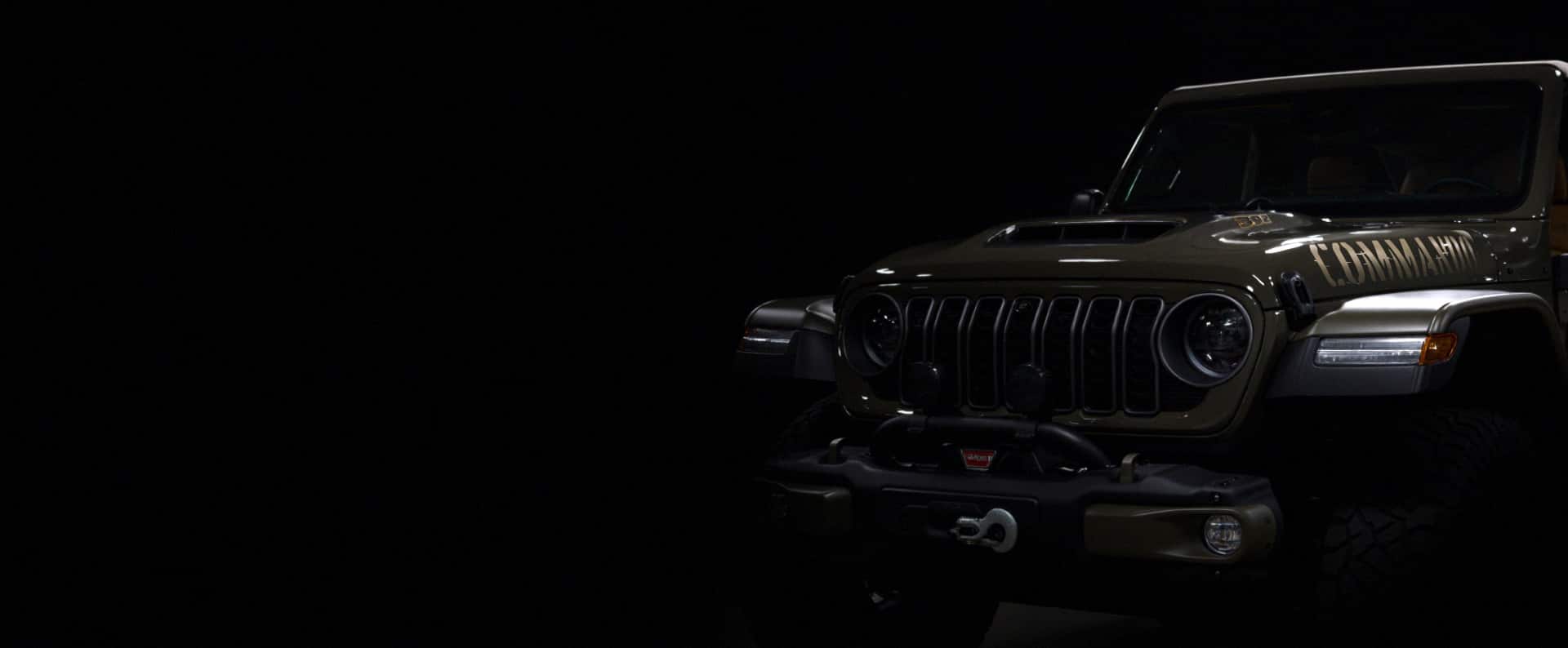 The front end of a drab olive green 2026 Jeep Wrangler Commando on a black background.