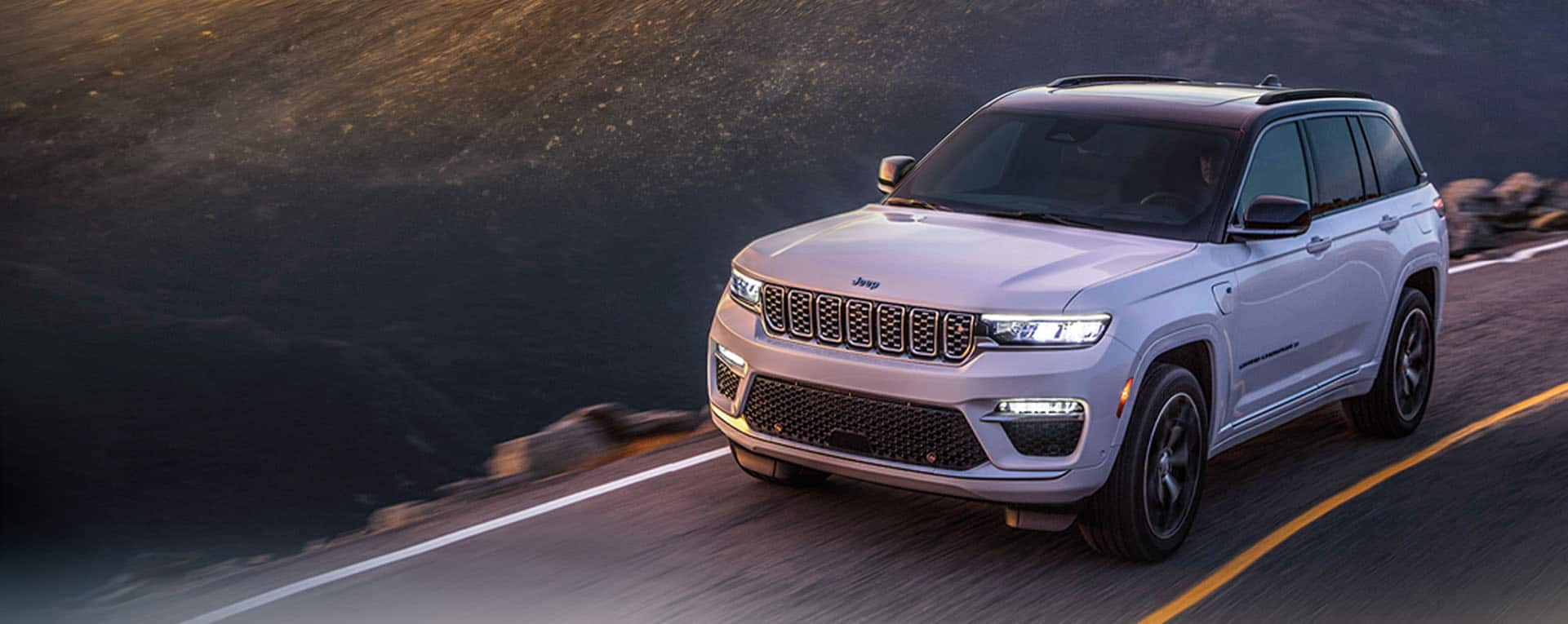 A white 2024 Jeep Grand Cherokee Trailhawk 4xe with a black hood insert, being driven off-road.