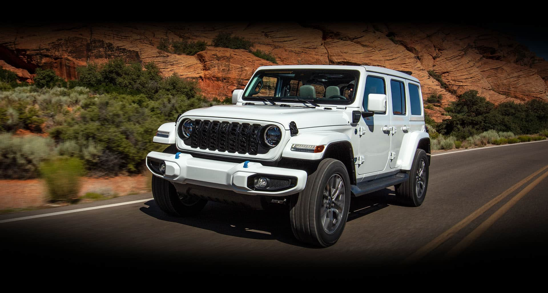 A white 2024 Jeep Wrangler High Altitude 4xe being driven on a mountain highway.