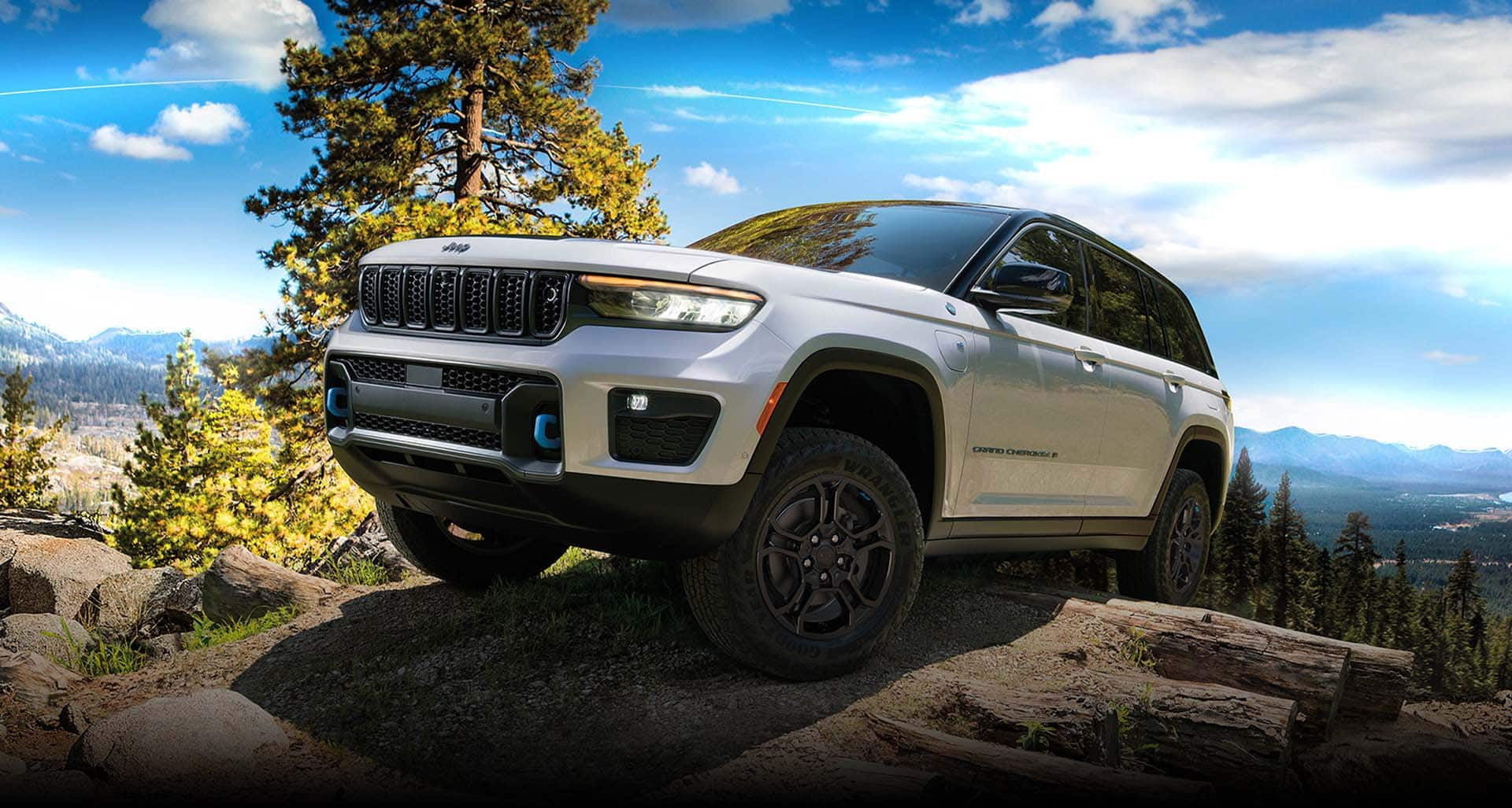 A white 2024 Jeep Grand Cherokee Trailhawk 4xe with a black hood insert, climbing a hill, off-road.