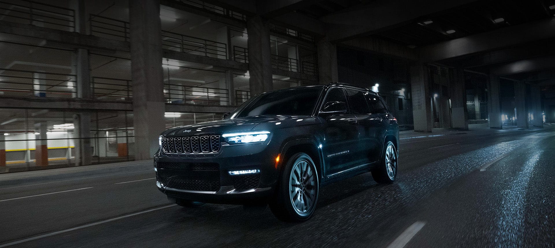 A black 2024 Jeep Grand Cherokee Summit Reserve traveling down a city highway at night.