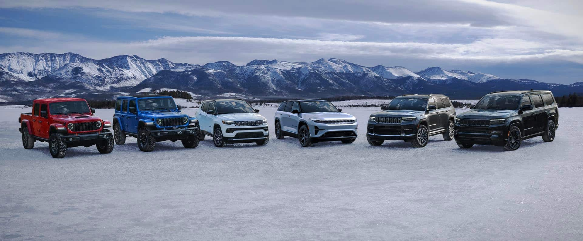 A lineup of six Jeep Brand vehicles parked in a semicircle on a snow-covered clearing in the mountains. From left to right: a red 2025 Jeep Gladiator Mojave X, a blue 2025 Jeep Wrangler Rubicon X 4xe, a white 2025 Jeep Compass Limited, a grey 2025 Wagoneer S, a black 2025 Grand Cherokee Summit Reserve and a black 2025 Jeep Grand Wagoneer Obsidian.