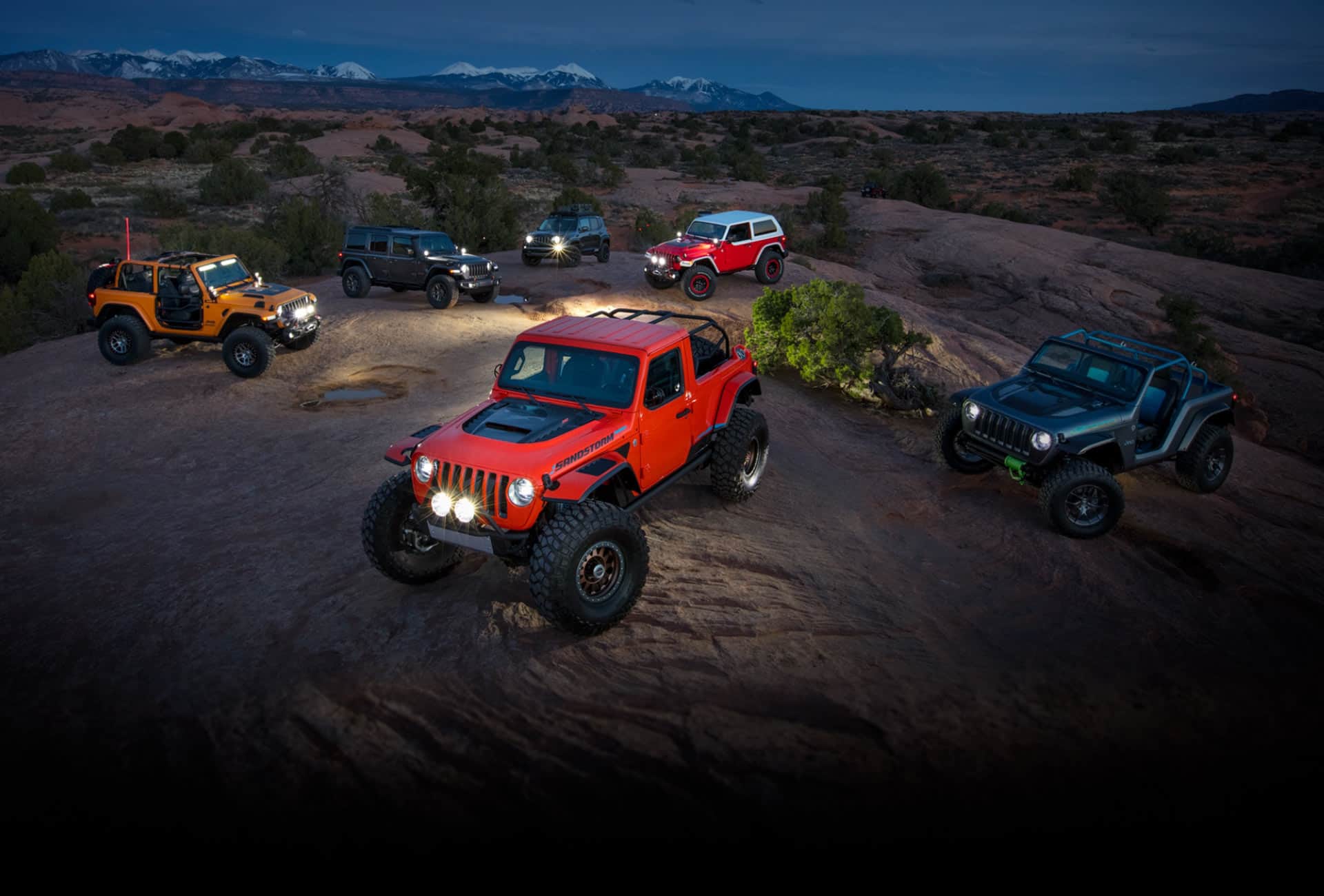A set of six Jeep Brand Concept vehicles parked on a hill in the desert at night.