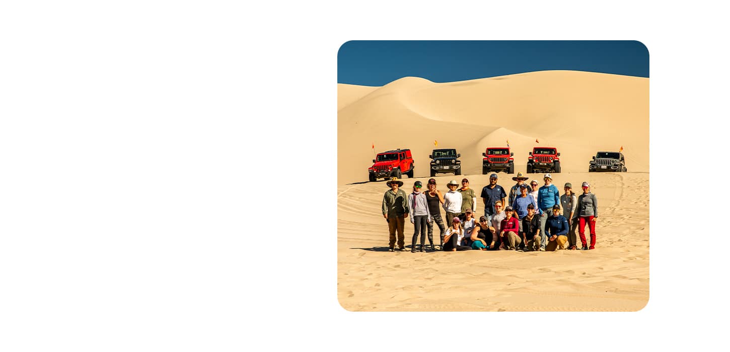 A Jeep Brand event in the desert with a group of Jeep Brand vehicle owners in the foreground and five Jeep Brand vehicles in the background.