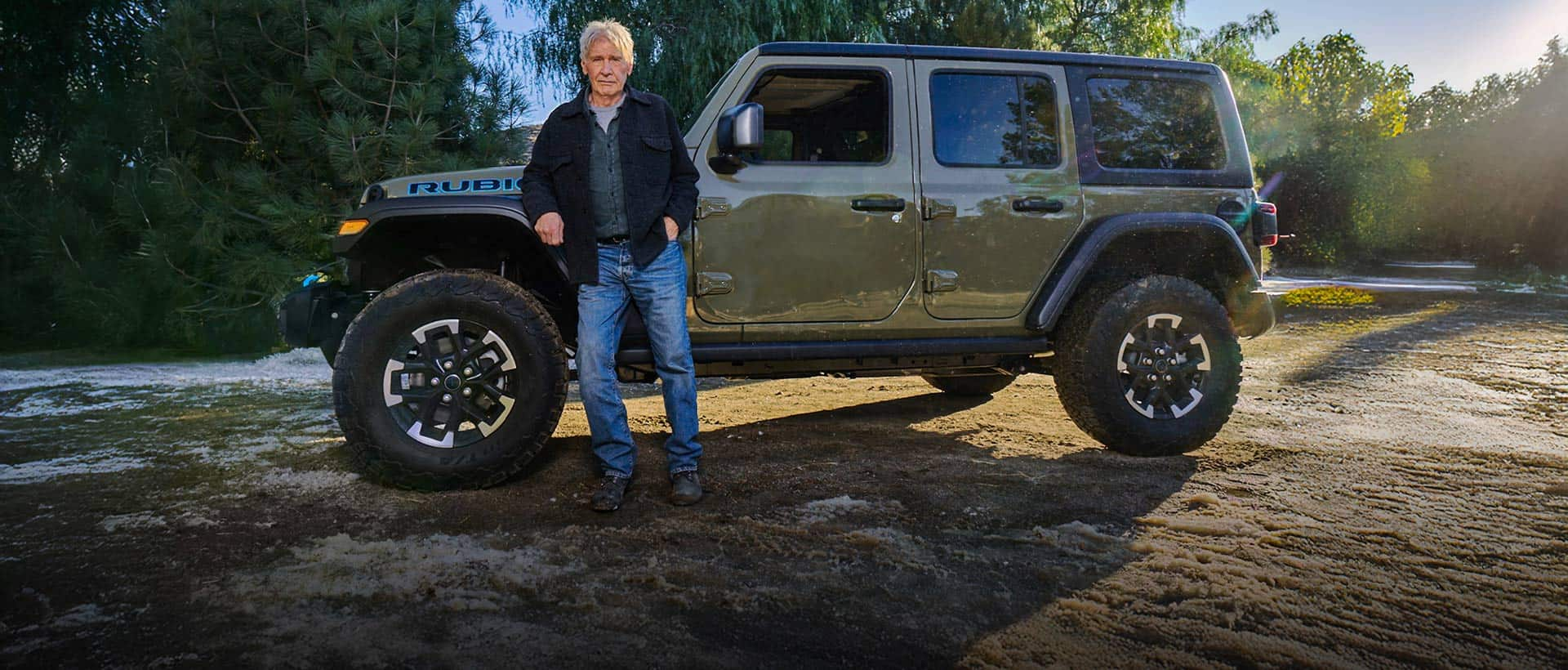 Harrison Ford standing beside an olive green 2025 Jeep Wrangler Rubicon 4xe.