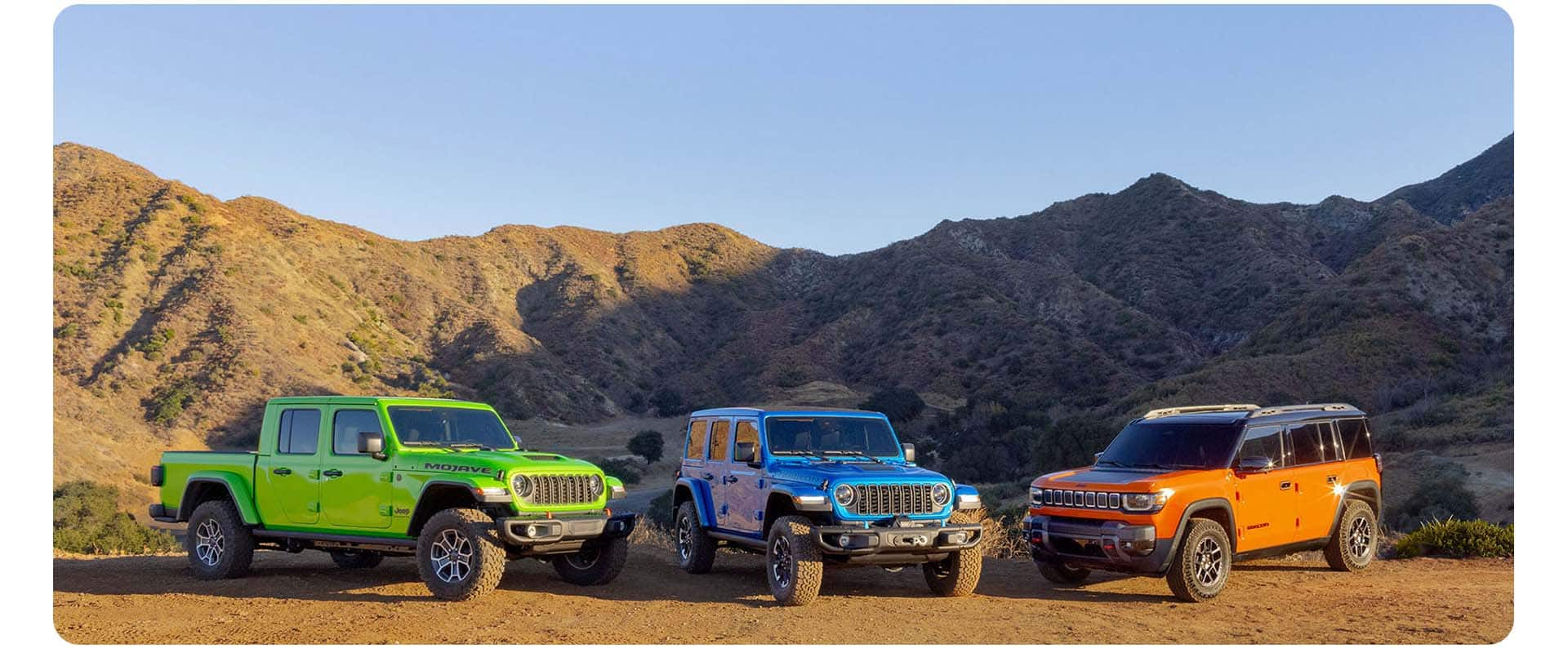 Three 2025 Jeep Brand vehicles on a clearing in the mountains. From left to right: A green Jeep Gladiator Mojave X, a blue Jeep Wrangler Rubicon X 4xe and an orange Jeep Recon preproduction model.