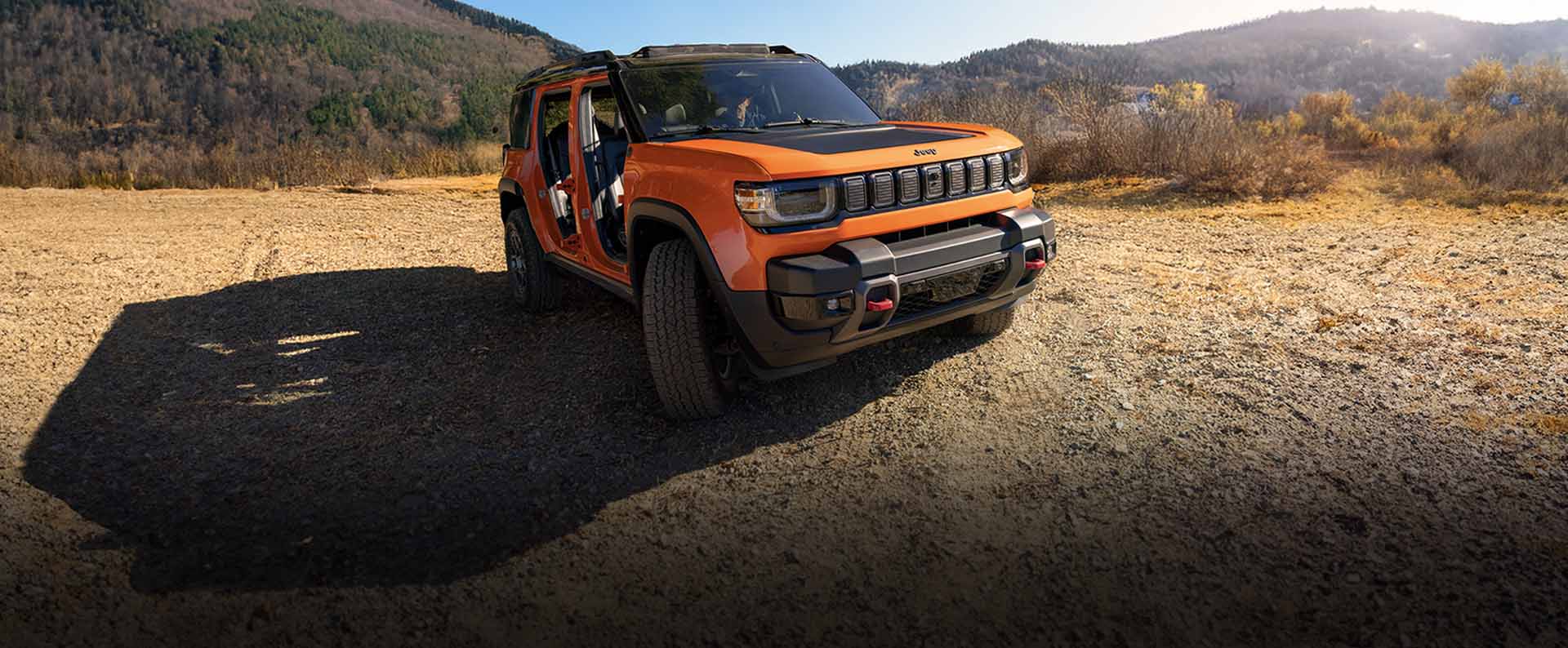 An orange 2025 Jeep Recon preproduction model with its doors removed, on a clearing in the mountains.