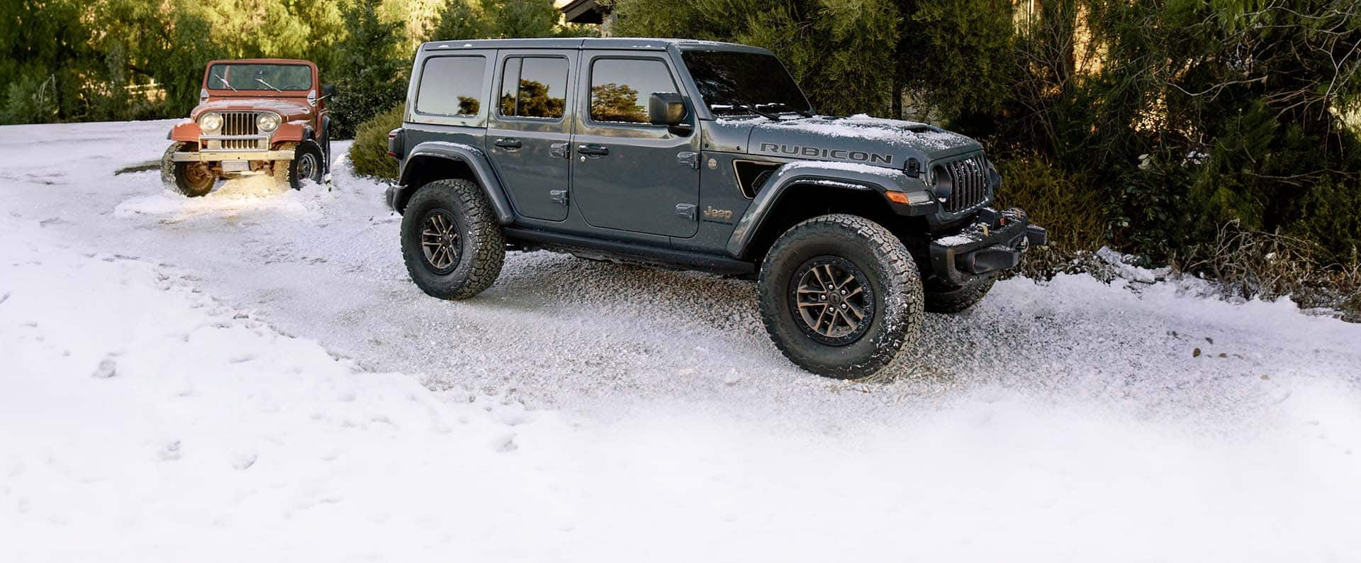 A gray 2025 Jeep Wrangler Rubicon 392 Final Edition traveling through a snow-covered trail, followed by a vintage red Jeep Wrangler.