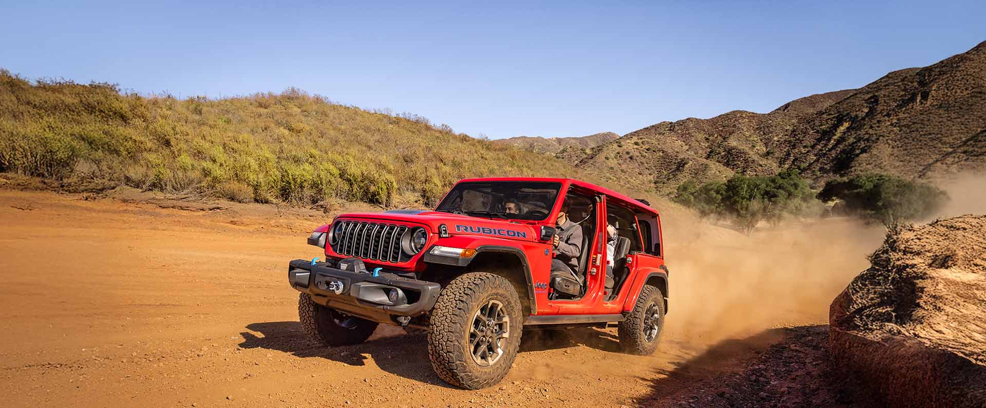 A red 2025 Jeep Wrangler 4xe Rubicon X 4xe with its doors removed, ascending a trail off-road.