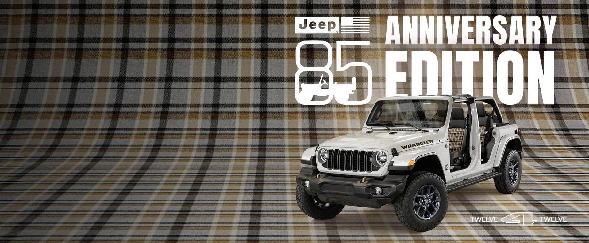 A driver-side front angle of a white 2026 Jeep Wrangler 85th Anniversary Edition with its doors and top removed, revealing plaid inserts on the front and rear seats, parked on a seamless plaid surface that extends up the wall behind it. Jeep 85 Anniversary Edition.