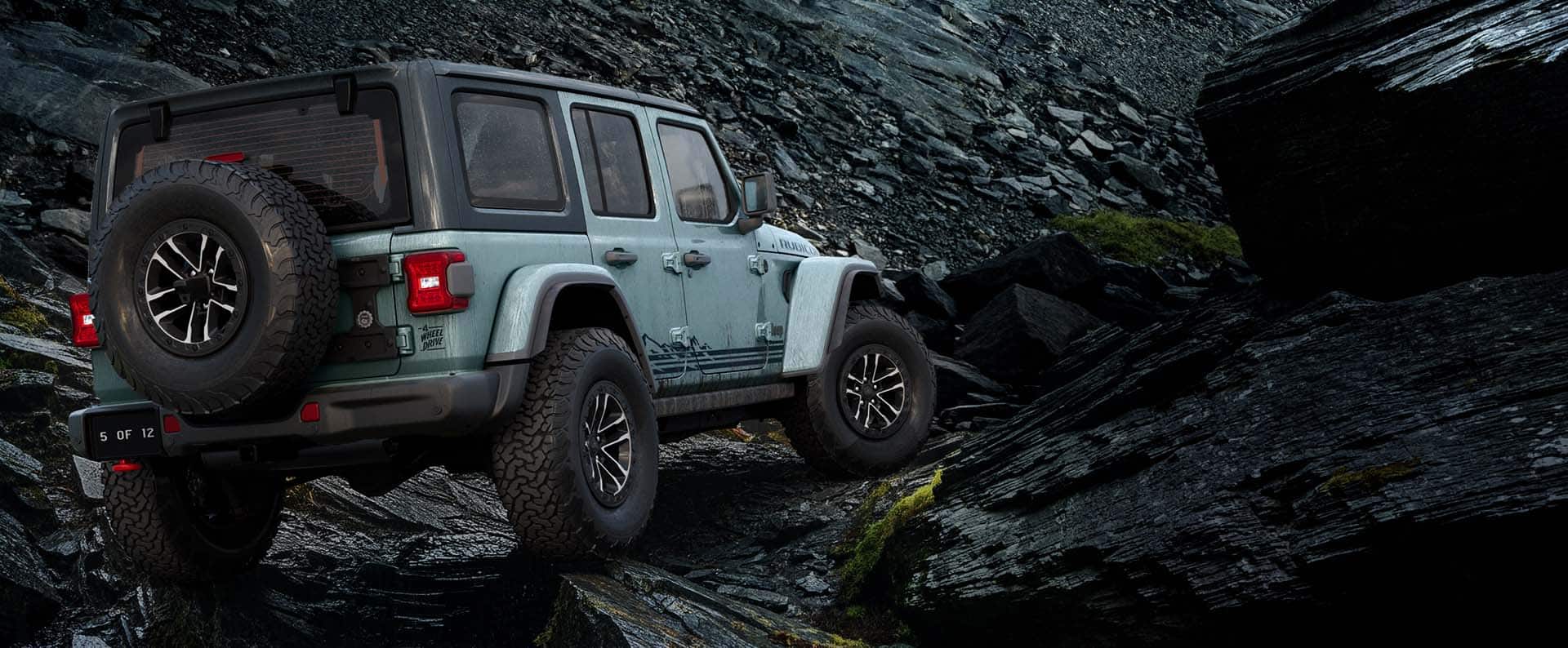 A passenger-side rear angle of a blue-green 2026 Jeep Wrangler Rubicon Rockslide crawling over a rocky trail off-road.