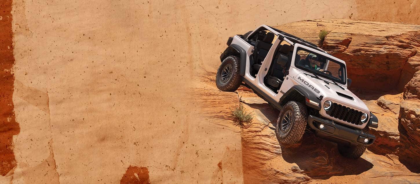 A white 2026 Jeep Wrangler Moab 392 with its doors and top removed, descending a huge rock formation.